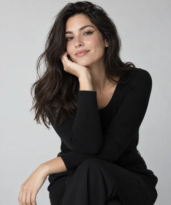 Retrato de estúdio de uma mulher confiante de cabelos escuros usando um look preto simples diante de um fundo cinza-claro, com fotografia de moda natural e refinada